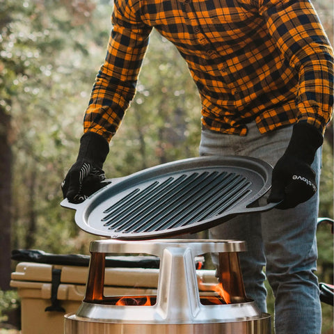 Person placing Large Cast Iron Grill Top For Bonfire And Yukon Fire Pit Outdoor Cooking Surface Seventeen And Three Quarters Inch 17 Lbs Fire Pit Accessory For Flame To Table Meals onto fire pit