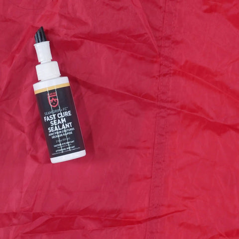 Seam Grip FC Fast Cure Sealant For Tents Rainflies Tarps And Awnings Water Based Seam Sealer 2 Fl Oz bottle on red fabric