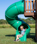 Child playing at the bottom of a spiral tube slide on Cedar Cove Wooden Swing Set With Spiral Tube Slide And Wave Slide