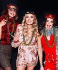 Three women wearing Mardi Gras Beads Necklaces 24 Pack, 33 Inch Round Beads In Green Purple Gold, at a festive party.