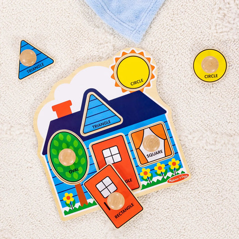 First Shapes Jumbo Knob Puzzle For Toddlers with Wooden Peg Pieces on a carpet, featuring house and basic shapes