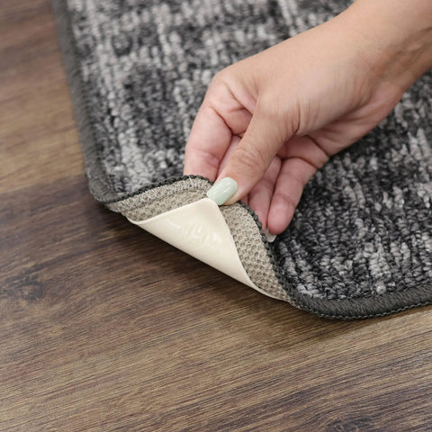 Hand applying Non Slip Corner Gripper Rug Tabs Eight Pack Anti Curling Double Sided Adhesive 4 Inch By 4 Inch Squares to rug corner