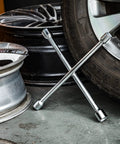 Heavy Duty Four Way Universal Cross Lug Wrench Tire Iron 14 Inch Long forged chrome plated steel on garage floor with tires.