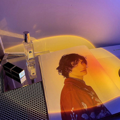 Sunset Projection Lamp With 180 Degree Rotation LED Night Light casting glow on perfume and magazine in bedroom decor