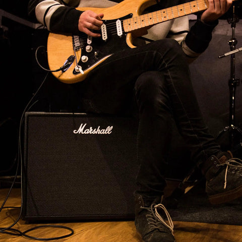 Person playing electric guitar with Marshall amp similar to Code50 Digital Guitar Amplifier With Fifty Watt Output One Hundred Plus Presets Twenty Four Digital Effects Fourteen Preamp Models Bluetooth Connectivity Three Point Five Millimeter Aux Input Versatile Tone For Practice Rehearsal And Live