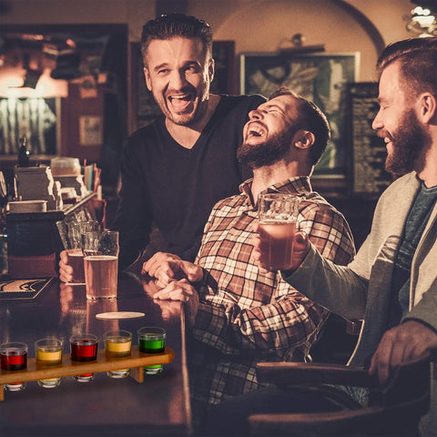 Kick Back Wooden Shooting Board Set With Eighteen Shot Glasses For Chill Game Nights at a bar with smiling friends.