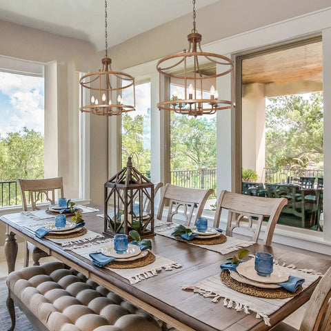 Dining room with two Rustic Bronze Farmhouse Six Light Drum Chandeliers over a wooden table set for a meal, cozy vibe.