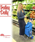 Woman shopping with Foldable Trolley Dolly Shopping Cart with blue bag, heavy-duty wheels, in a grocery aisle full of vegetables.