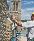 Worker applying The Real Deal Deep Penetrating Siloxane Masonry Sealer For Brick Concrete And Stucco on a stone wall.
