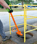 Compact Magnetic Lid Lifter That Cracks Open Tough Manhole Covers Without Breaking A Sweat While Hauling Up To 150 Pounds Thanks To Strong Neodymium Magnets And Solid Aluminum Frame In Orange being used to lift a manhole cover.