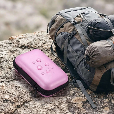 Pink EVA Hardshell Gadget Organizer Pouch With Cord Holder For Travel Electronics Storage on rocky surface near backpack.