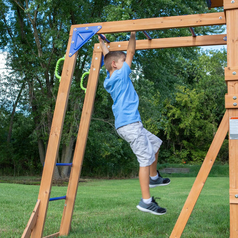 Child using monkey bars on Beachfront Cedar Wood Swing Set With Wave Slide Elevated Deck Canopy Monkey Bars Rock Wall Ladder