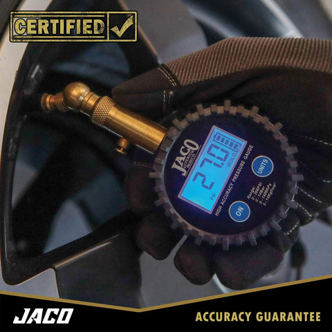 Front view of JACO Elite digital tire pressure gauge with brass air chuck and blue LCD display, held by a gloved hand.