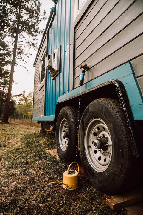 Tap Water Filtration System With 0.1 Micron Inline Filter attached to blue RV hose bib, yellow watering can below, outdoor setting