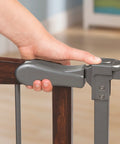 Close-up of hand operating Walk Through Baby And Pet Gate With Walnut Wood And Charcoal Metal Accents, easy grip handle shown.