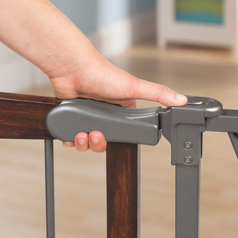 Close-up of hand operating Walk Through Baby And Pet Gate With Walnut Wood And Charcoal Metal Accents, easy grip handle shown.