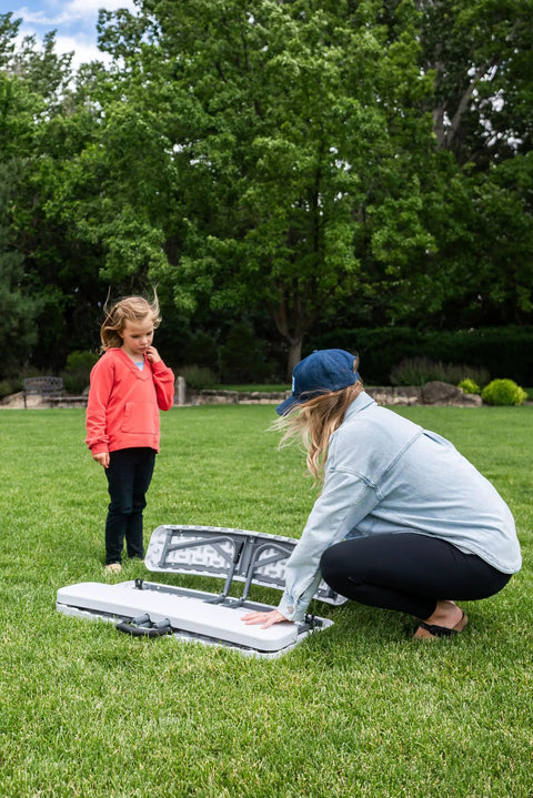 Adult and child setting up Compact Kids Picnic Table With Foldable Benches Under The Table And Built In Carry Handle For Easy Transport on grass