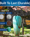 Outdoor Antique Jar Water Fountain With LED Lights 33 Inch Turquoise Cascading Water Feature For Garden Patio And Yard Decor Cool Night Glow And Tranquil Backyard Vibe next to park bench with blooming tree in background.