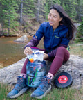 Person using BV475 Trek Portable Bear Resistant Canister For Backpackers next to a river while camping outdoors