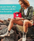 First aid kit, red with white cross emblem, held by person on rocky shoreline.