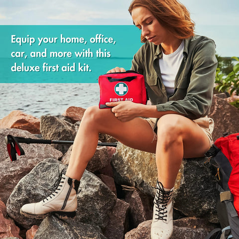 First aid kit, red with white cross emblem, held by person on rocky shoreline.