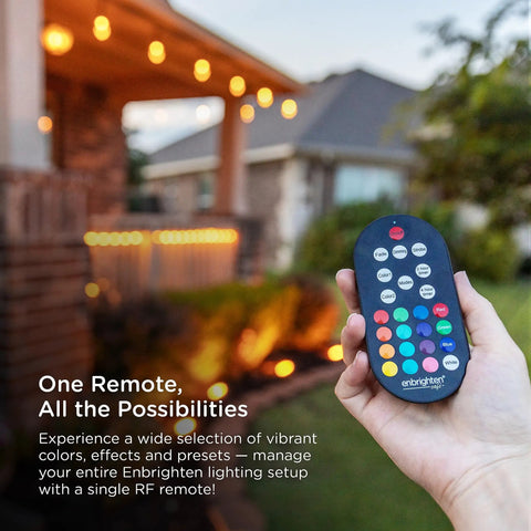 Hand holding RF remote in front of lit patio; Vintage Outdoor String Lights 24ft With 12 RGB Acrylic Bulbs visible in background.