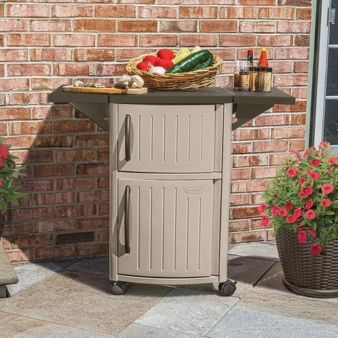 Outdoor Grilling Prep Station With Storage Portable Backyard Kitchen Counter Durable Resin Weather Resistant Top Cabinet For Serving Tray And More With Drop Leaf Extensions Taupe Brown in a garden setting with food items on top.