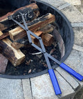 Heavy Duty Collapsible Firewood Tongs 28 Inch Solid Manganese Steel With Serrated Scissor Jaws beside logs in a fire pit.
