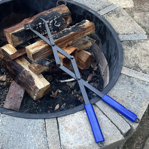 Heavy Duty Collapsible Firewood Tongs 28 Inch Solid Manganese Steel With Serrated Scissor Jaws beside logs in a fire pit.