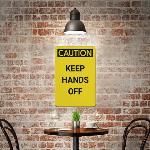 Keep Hands Clear Caution Sign 8x12 Aluminum UV Safety Plaque displayed against a brick wall under a hanging light, above a table.