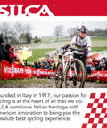 Cyclist carrying bike in muddy race with crowd and sponsor banners visible in background, promoting cycling heritage and innovation.