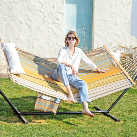 Person relaxing on waterproof double hammock with stand, 55 inch hardwood spreader bar, quick dry Textilene fabric in outdoor setting.