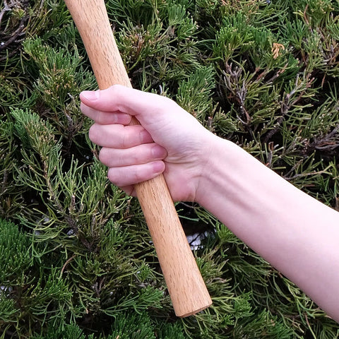 Hand holding wood handle of Beast Of A Heavy Duty Japanese Hand Forged Steel Pick Axe For Digging And Weeding Gardens