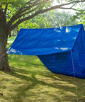 A blue tarp set up as a shelter between trees using the CamJam Cord Tightener 4 Pack Easy Knot Free Rope Tensioner.