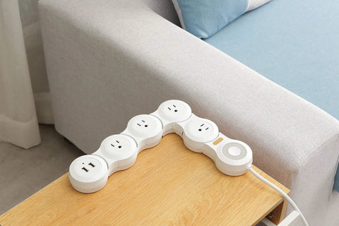 Flexible Surge Protector Power Strip With 6 Foot Cord 4 Outlets 2 USB Ports Overload Protection Flat Plug Rotatable 180 Degree Design For Tight Spots Ideal For Home Office And Travel White placed on a wooden table next to a couch