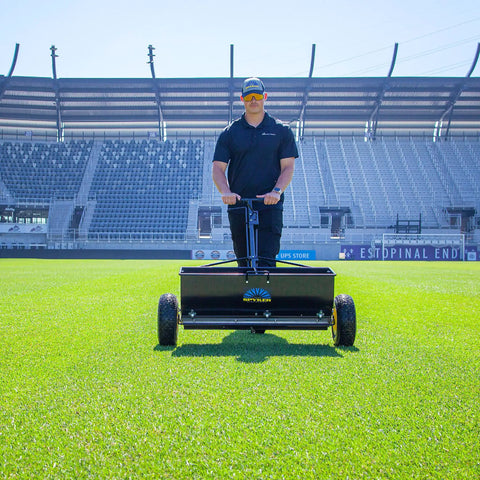 Person using Spyker P70-12010 Commercial Drop Spreader With 120 Lb Hopper, 36 Inch Spread Width, on stadium lawn.