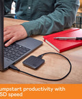 2TB Portable SSD With USB 3 For Quick File Transfers On The Go connected to a laptop, red notebook nearby