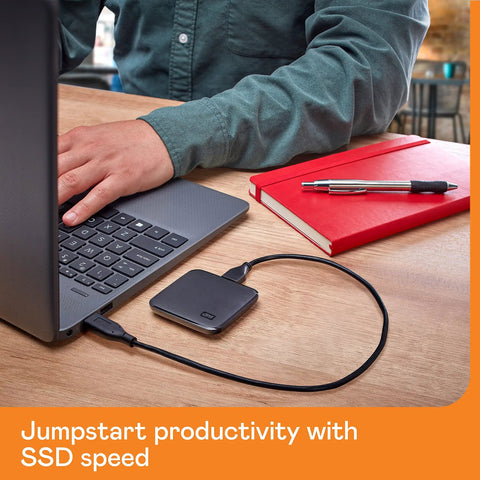 2TB Portable SSD With USB 3 For Quick File Transfers On The Go connected to a laptop, red notebook nearby