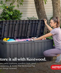 Woman opening 92 Gallon Resin Deck Box in dark gray for outdoor storage, showing pool floats and cushions inside on a patio