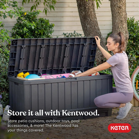 Woman opening 92 Gallon Resin Deck Box in dark gray for outdoor storage, showing pool floats and cushions inside on a patio