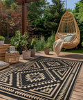Reversible Waterproof Outdoor Rug 5x8 Ft for Patio Deck with Black and Brown Geometric Pattern, shown on a wooden deck with plants.