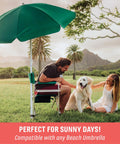Director Style Outdoor Chair With Side Table And Armrest Caddy set in a grassy field with beach umbrella, man and woman, dog nearby