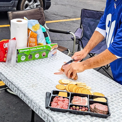 Person using EZ Board Disposable Plastic Cutting Board For Quick Cleanup And Easy Food Prep On The Go for slicing salami at a picnic.