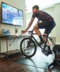 Cyclist using front wheel block with indoor bike trainer in living room for realistic ride, 11x5x4 inch riser for alignment.