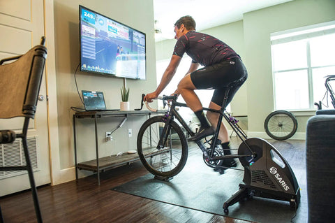 Cyclist using front wheel block with indoor bike trainer in living room for realistic ride, 11x5x4 inch riser for alignment.