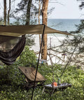 Kompound Camping Hammock With Net And Warm Internal Cover Ultralight Portable Hammock set up by a beach under a tarp, in OD Green.