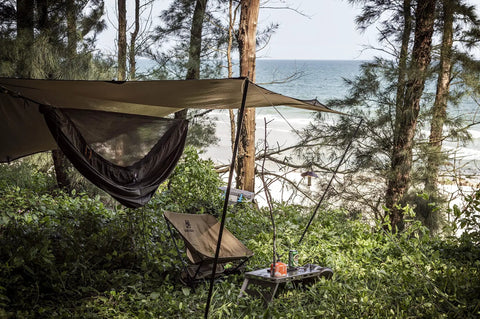 Kompound Camping Hammock With Net And Warm Internal Cover Ultralight Portable Hammock set up by a beach under a tarp, in OD Green.