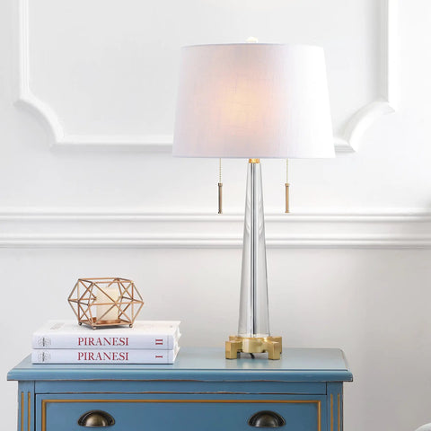 Crystal LED Table Lamp In Clear And Brass Gold Finish, 29.5 Inch Two Light Contemporary Glam Bedside Lamp With White Linen Drum Shade, Pull Chain, Energy Saving Bulbs Included, Perfect Living Room Accent on a blue table.