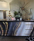 Modern dresser with abstract black and gold design, decor accents, and lamp in a stylish room setting