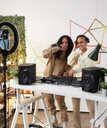 Two people DJing at a setup with DM-50D Active 5-Inch Desktop Monitor Speaker Built For Home Studio And Club DJ Sets